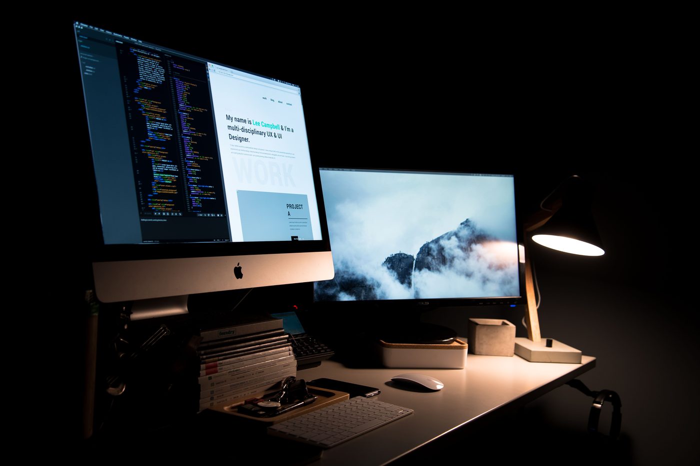 A designer's desk at night with a website and code editor open across two screens